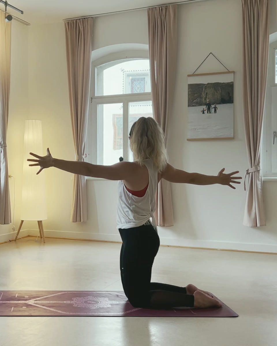 Yoga in Wangen im Allgäu: Eli kniet im hellen Kursraum auf der Yogamatte und öffnet die Arme weit